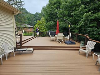 Back deck with tan railing, patio chairs, red umbrella, and a person in the distance