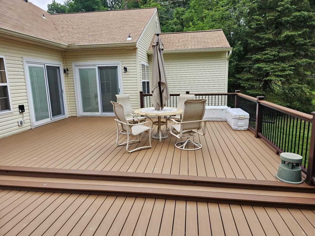 Wooden deck with patio table, chairs, closed umbrella, sliding doors, and forested backyard view