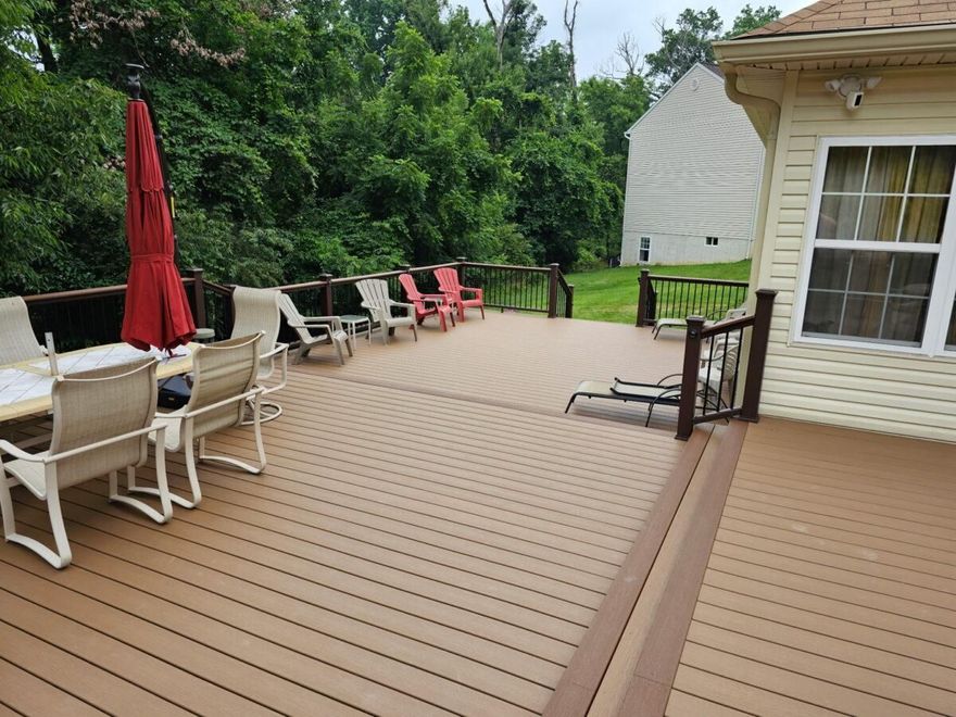 Back deck with patio chairs, red umbrella, and green backyard beside a house
