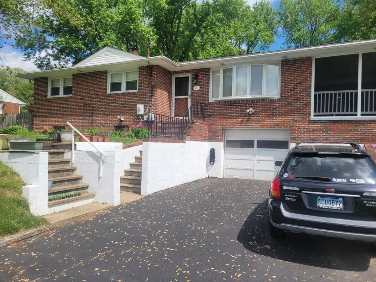 Brick suburban house with front steps, white railings, and a black SUV parked in the driveway