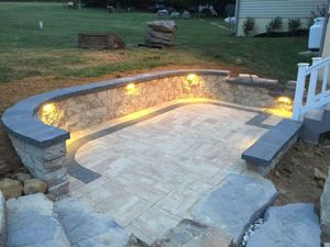 Stone patio with curved retaining wall and warm built-in lights in a backyard