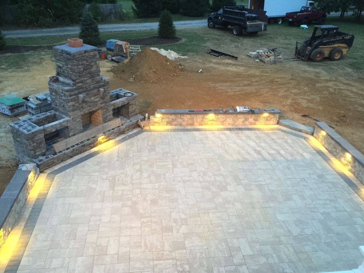 Backyard patio with light stone pavers and warm built-in steps, surrounded by construction materials at dusk