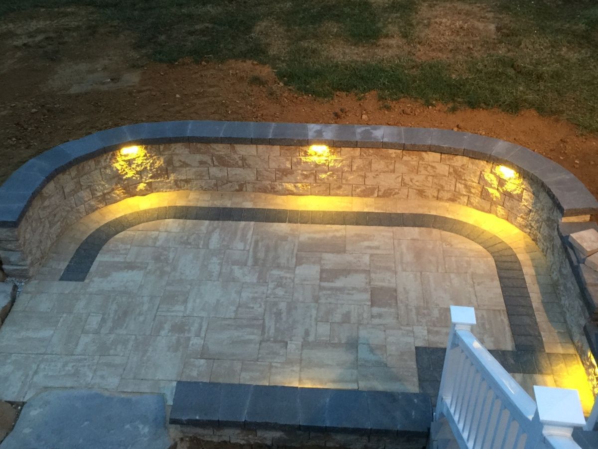 Stone patio with curved retaining wall and warm outdoor lights at dusk