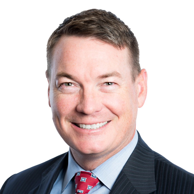 Smiling man in a dark suit, light blue shirt, and red tie against a white background
