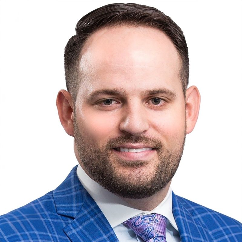 Headshot of a smiling man in a blue checkered suit and purple tie on a white background