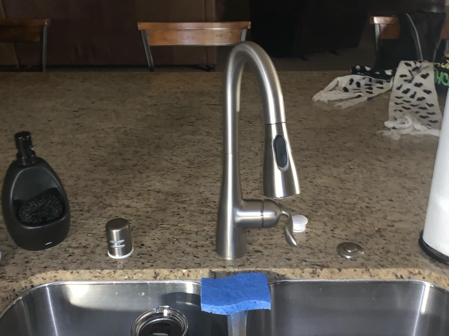 Kitchen sink with chrome faucet, blue sponge, dish soap, and a black cup on the counter.