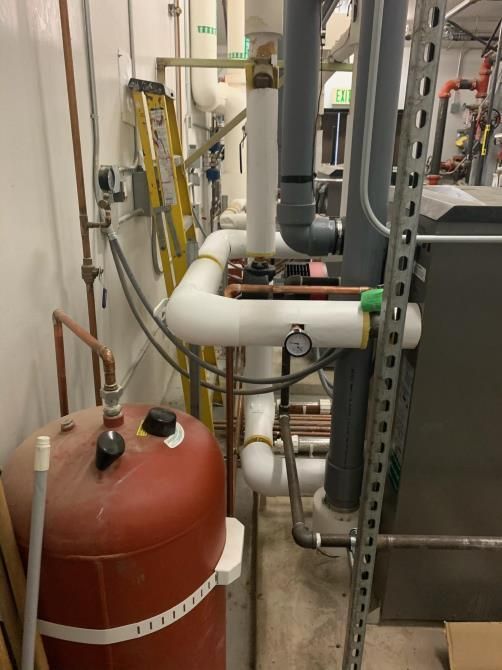 Industrial equipment room with red tank, white pipes, gray ductwork, and a yellow ladder.