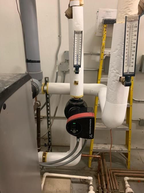 Industrial pipes and a black pump with red accents in a utility room