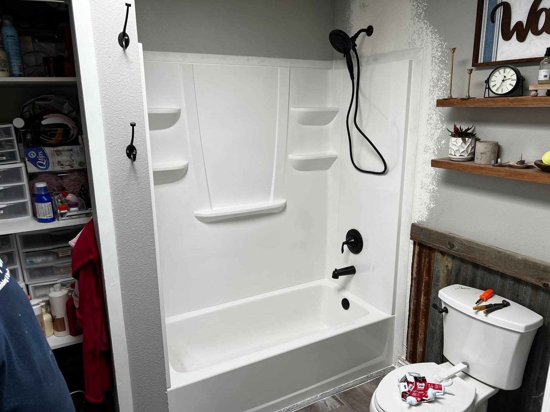White walk-in shower with built-in seat and shelving in a bathroom, beside a toilet and wooden wall shelves.