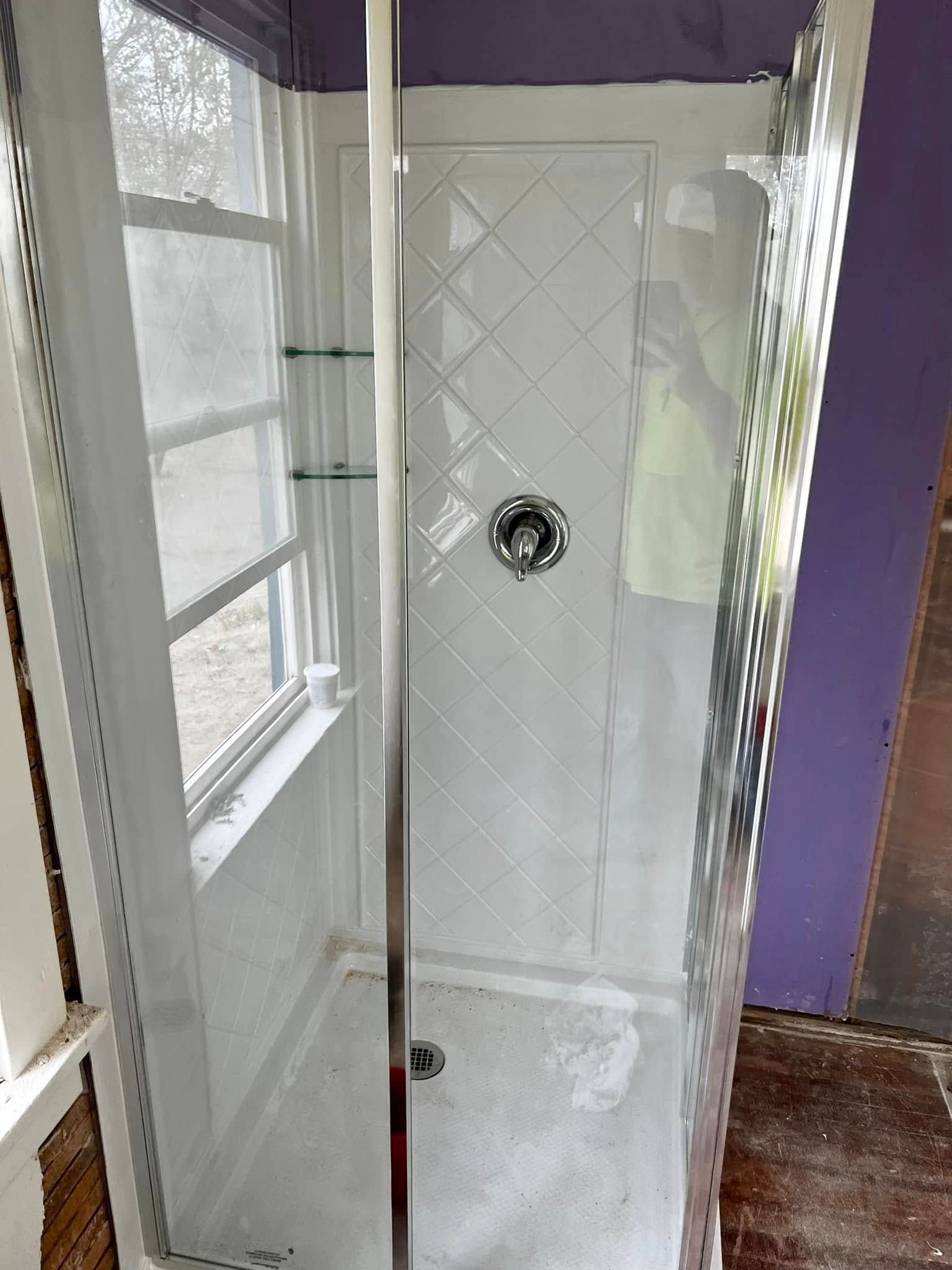 White shower stall with tiled walls, chrome showerhead, and a glass door in a bathroom