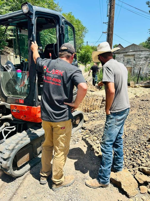 Two men inspect a compact excavator at a dusty construction site.