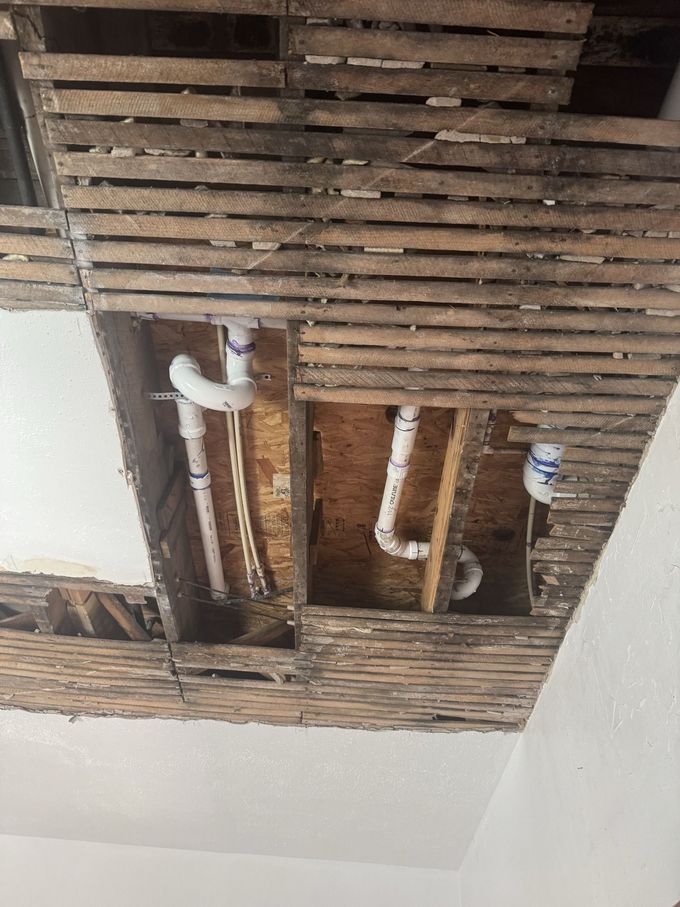 Ceiling with exposed wooden slats and plumbing pipes, showing damage or unfinished repair work