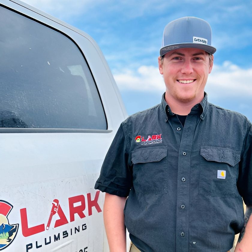 Smiling technician beside white service truck with red “ARK” plumbing logo under blue sky