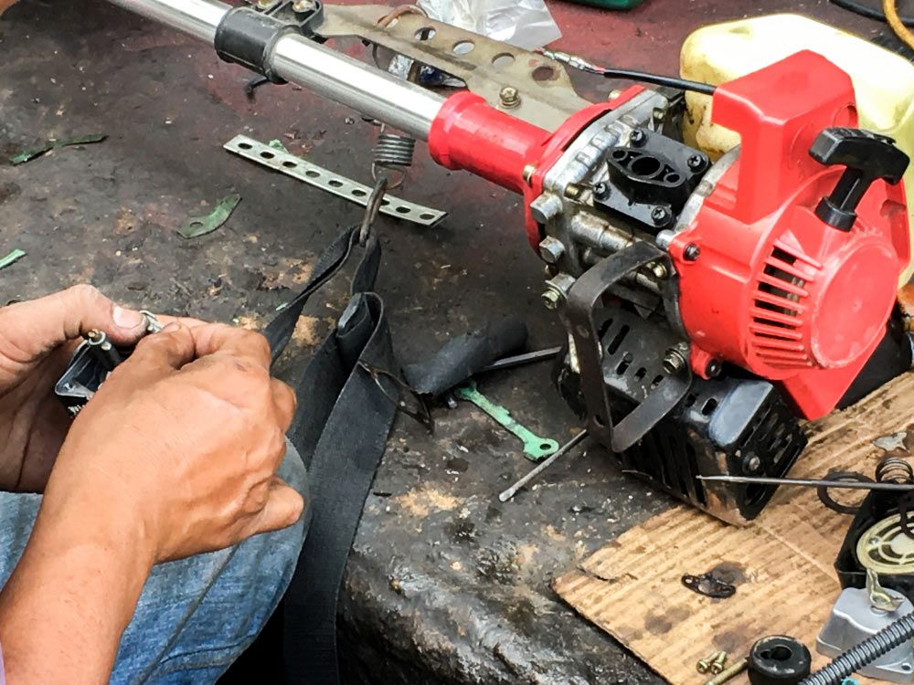 A Man is Fixing a Chainsaw With a Screwdriver — Ken Mills Machinery in Kingaroy, QLD