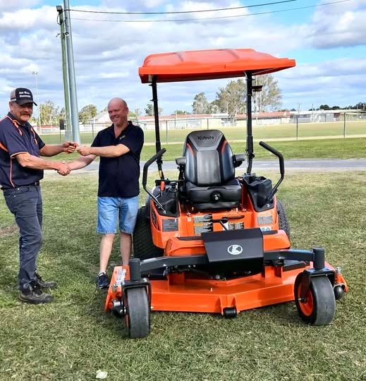 Two Men Shaking Hands Beside an Orange Riding Lawn Mower on Grass — Ken Mills Machinery in Mundubbera, QLD