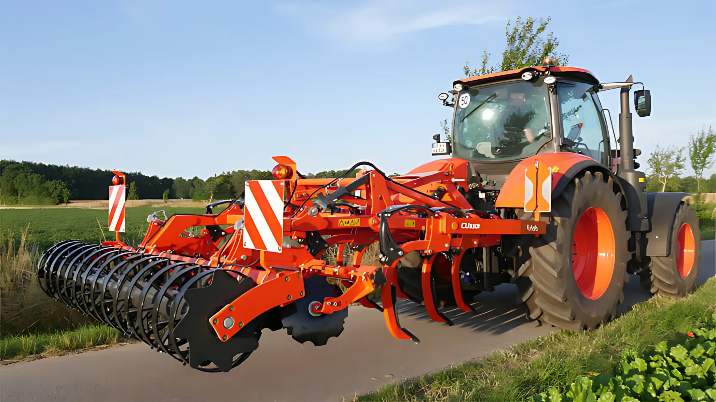 A red and orange tractor is driving down a road next to a field. — Ken Mills Machinery in Kingaroy, QLD