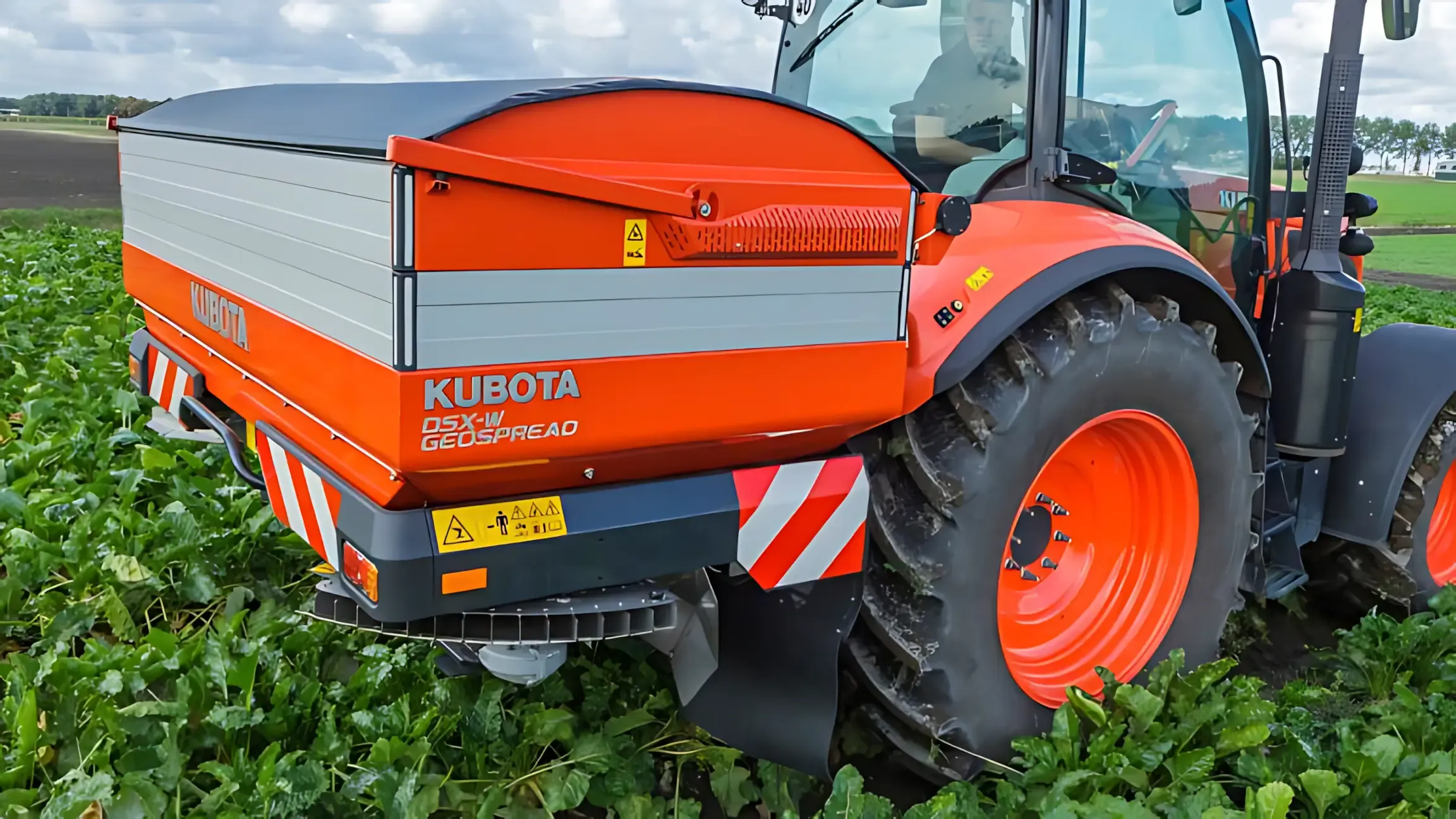 A red and black tractor is driving through a field of green plants. — Ken Mills Machinery in Kingaroy, QLD