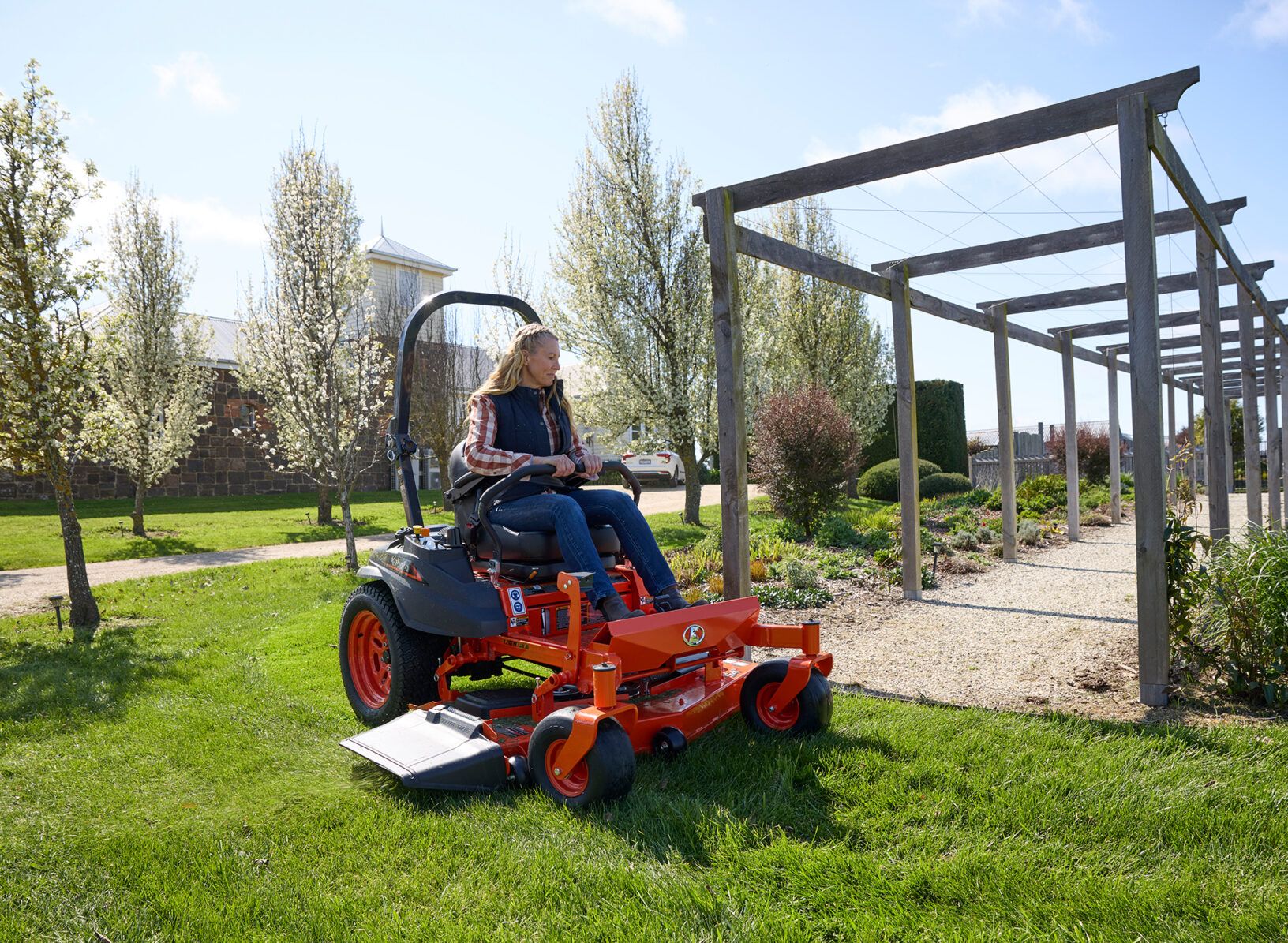 Person Rides an Orange Mower on a Grassy Path Beside a Pergola in a Park — Ken Mills Machinery in Nanango, QLD
