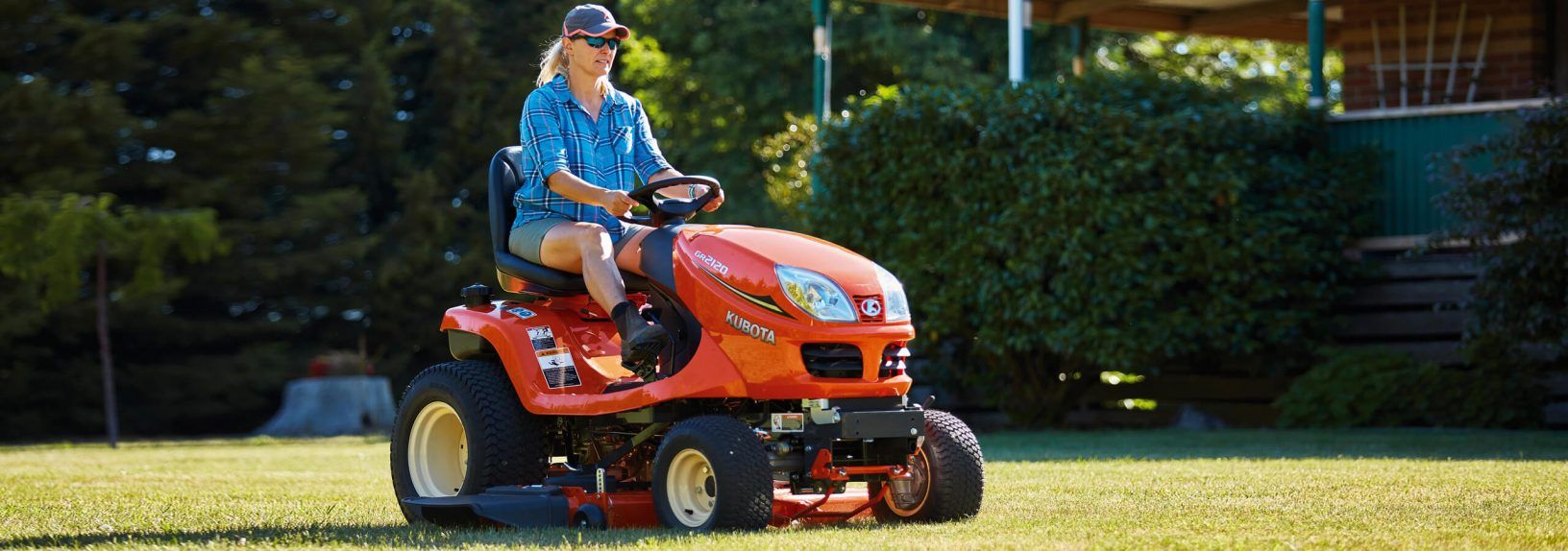 Person Riding an Orange Riding Lawn Mower on a Grassy Yard Near a Hedge — Ken Mills Machinery in Nanango, QLD
