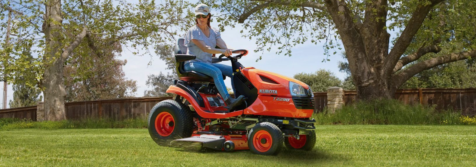 Person Mowing a Grassy Lawn on an Orange Riding Mower Under Trees — Ken Mills Machinery in Monto, QLD