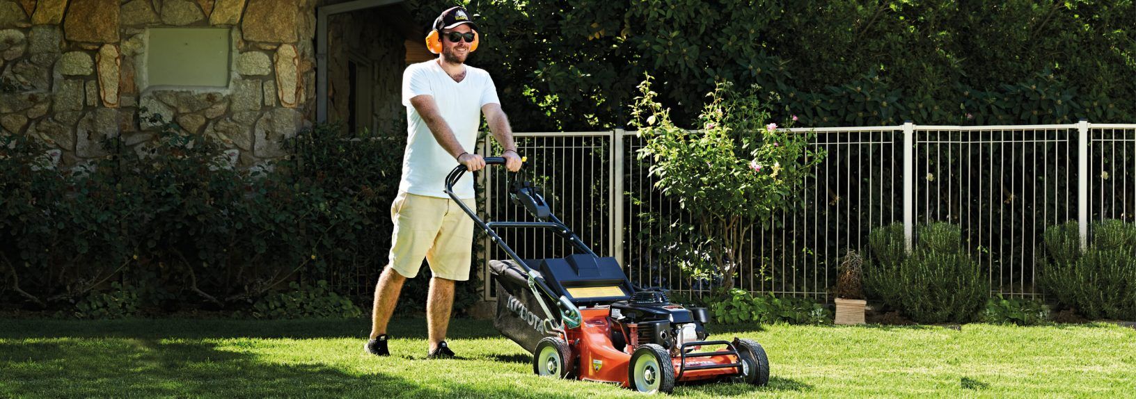 Person Mowing a Grassy Lawn With a Red Push Mower Near a Fence — Ken Mills Machinery in Mundubbera, QLD