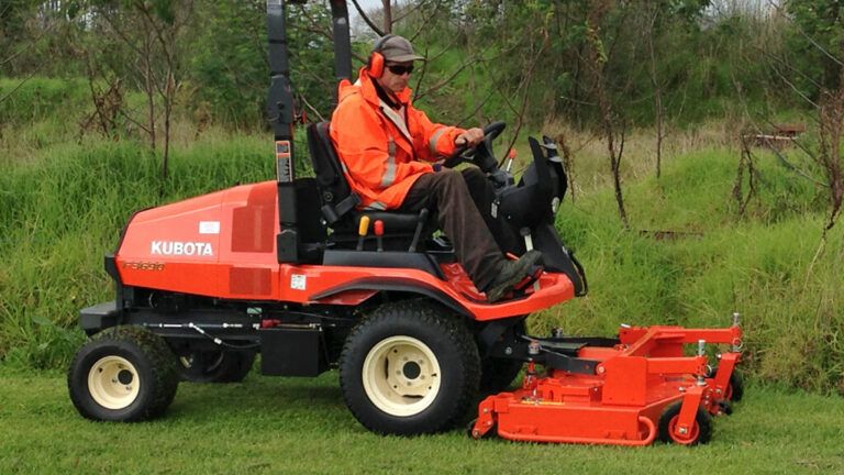 Person on a Red Kubota Riding Mower Mowing Grass in a Green Field — Ken Mills Machinery in Monto, QLD