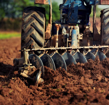 A tractor is plowing a dirt field with a license plate that says ' agricultural ' on it — Ken Mills Machinery in Kingaroy, QLD