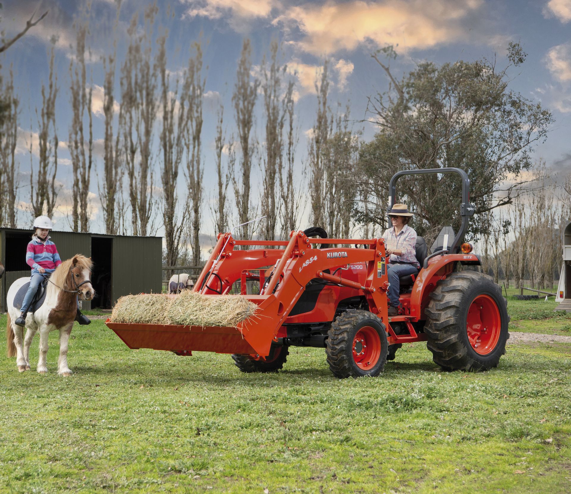 A Red Tractor With a Front Loader is Parked in a Grassy Field — Ken Mills Machinery in Kingaroy, QLD