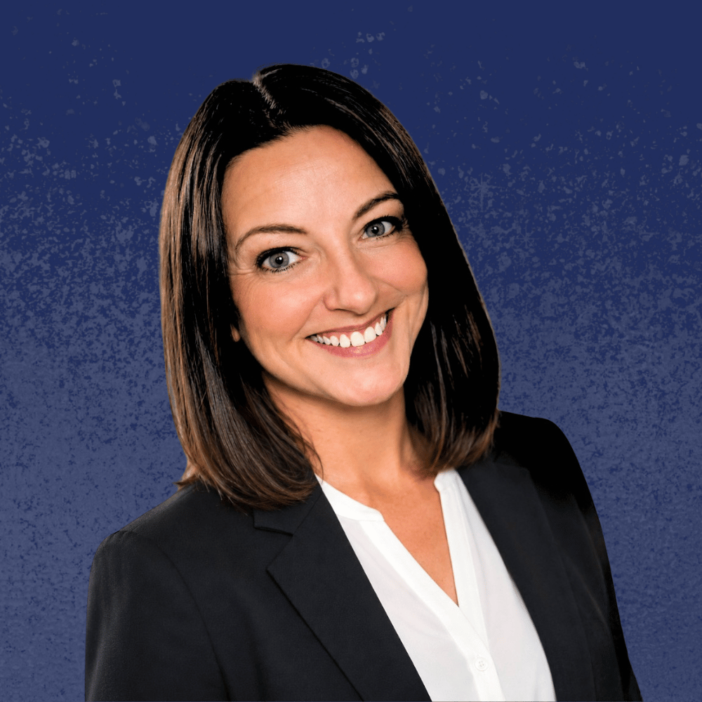 Smiling woman in a black blazer and gray top against a blue background.