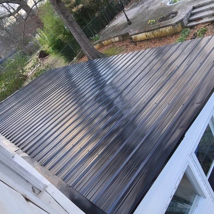 Angled view of a dark corrugated metal roof with white trim and nearby trees