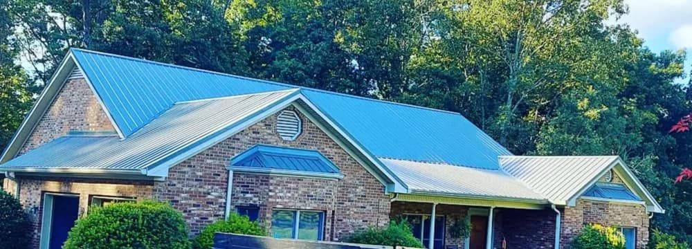 Brick house with blue metal roof and white columns surrounded by trees
