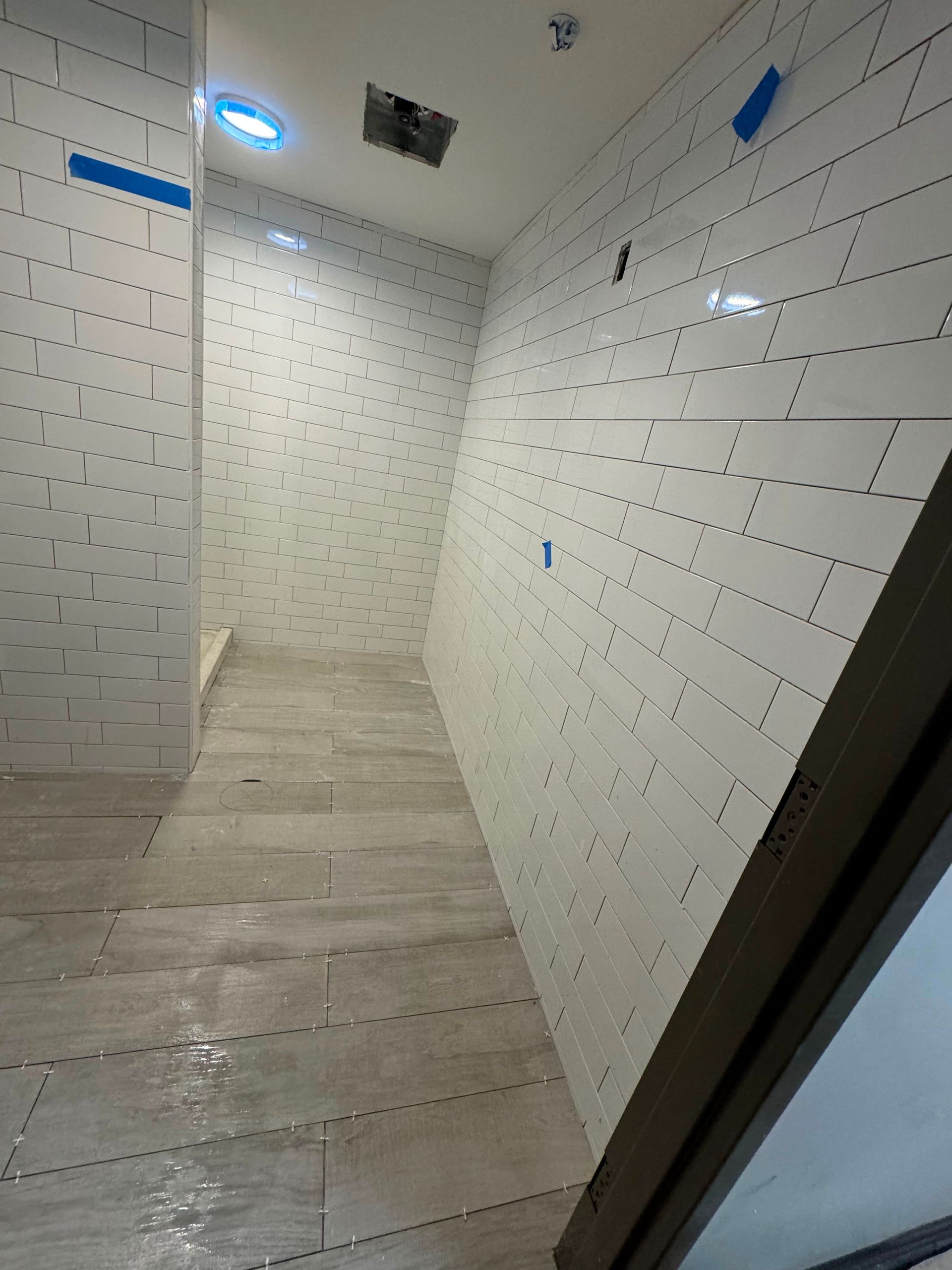 Empty tiled shower or bathroom with white walls and beige floor, viewed through an open doorway.