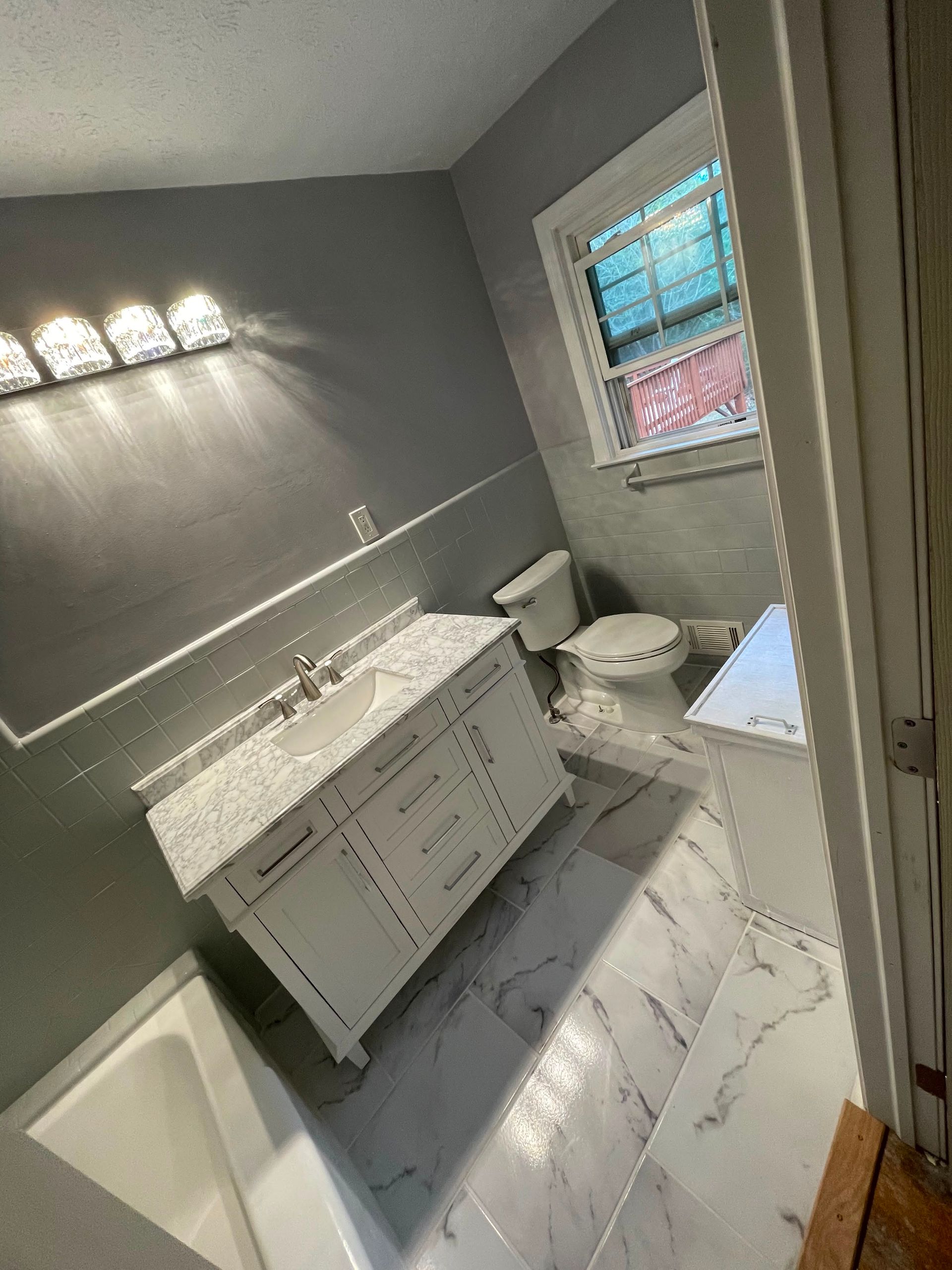 Small gray bathroom with double vanity, white tile floor, and window above the toilet.