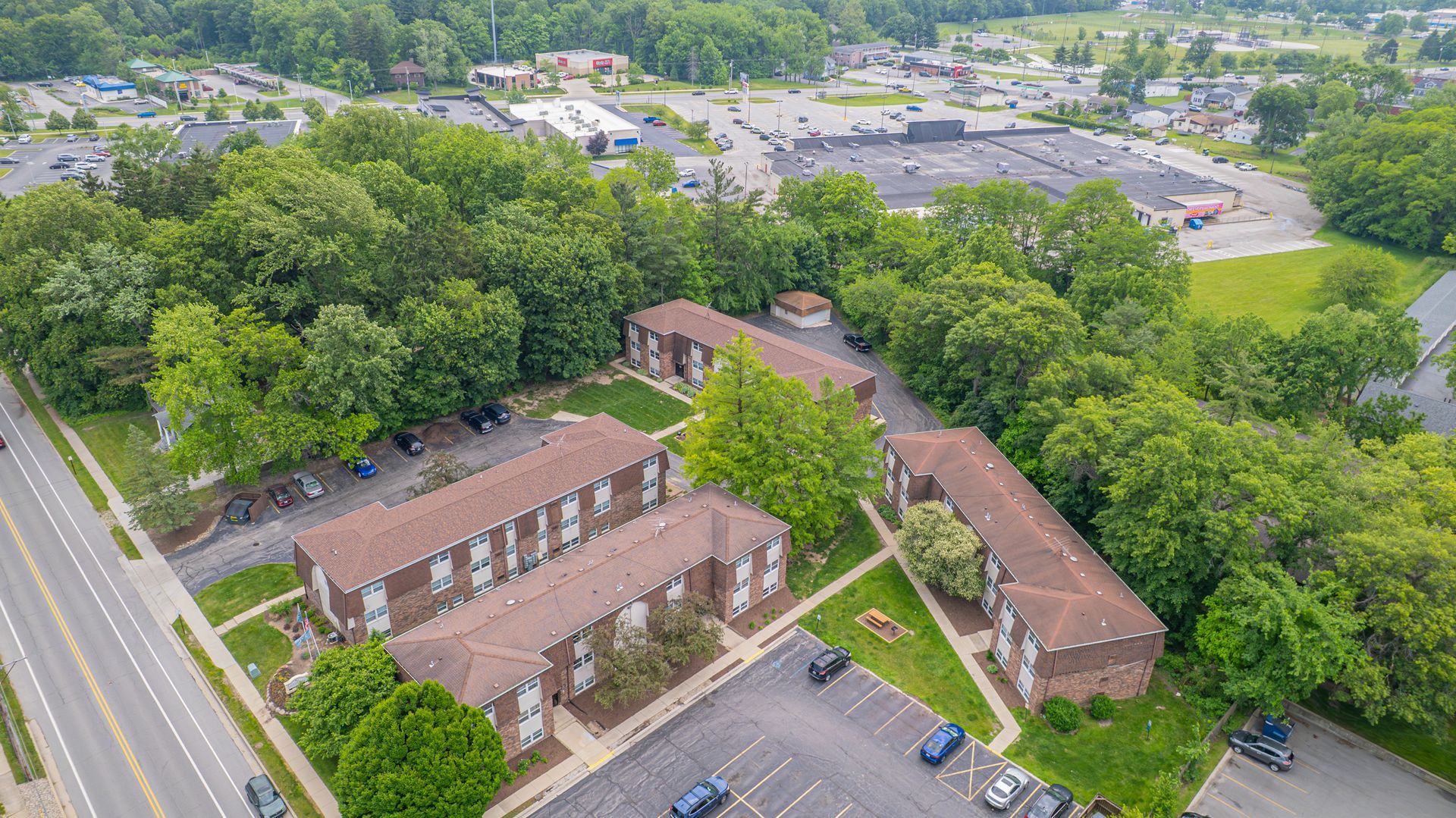 Aerial view of apartment buildings surrounded by trees and a parking lot.