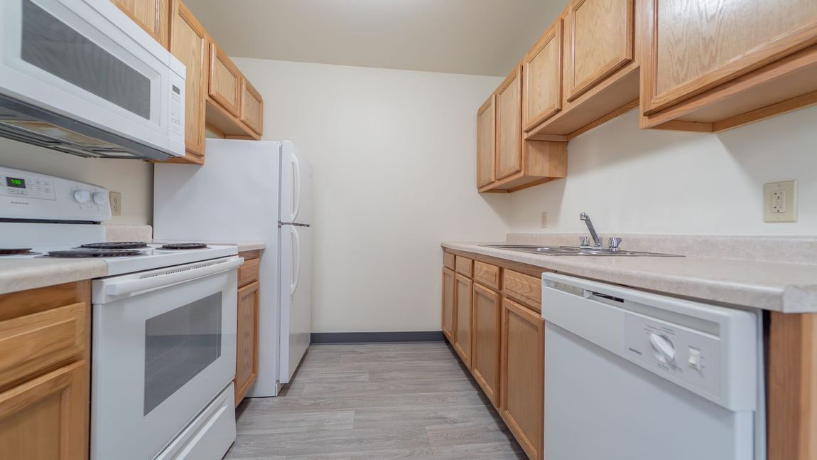 Kitchen with white appliances, wooden cabinets, and a light-colored countertop.