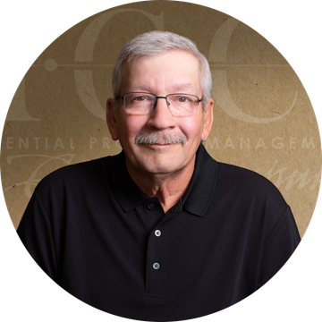Man with gray hair and glasses wearing a black shirt, smiling in front of a neutral backdrop.