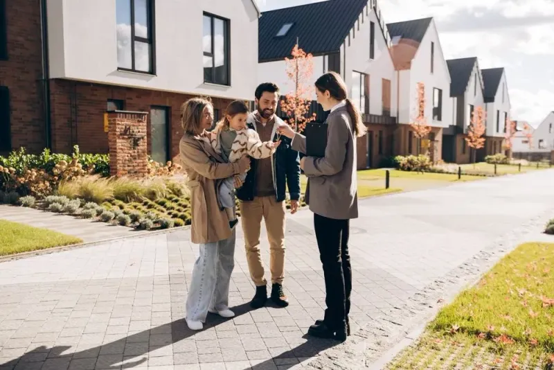 Three people discussing a brochure on a sunny residential street outside modern houses