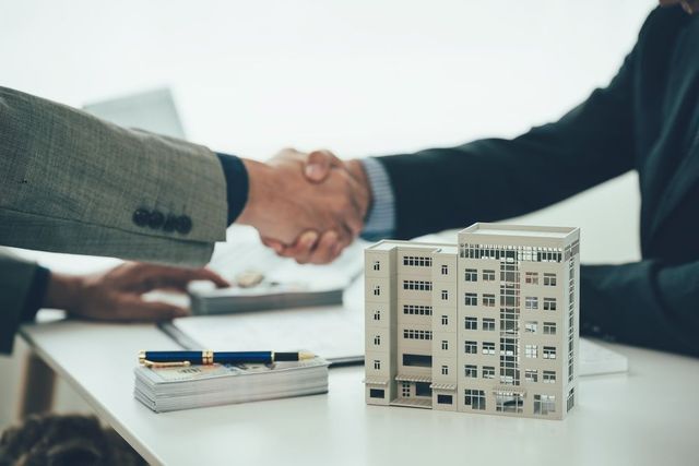 Businesspeople shaking hands beside a small model building on a desk
