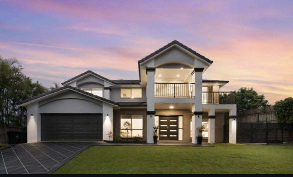 Modern two-story house with a large lawn, garage, and lit windows at sunset