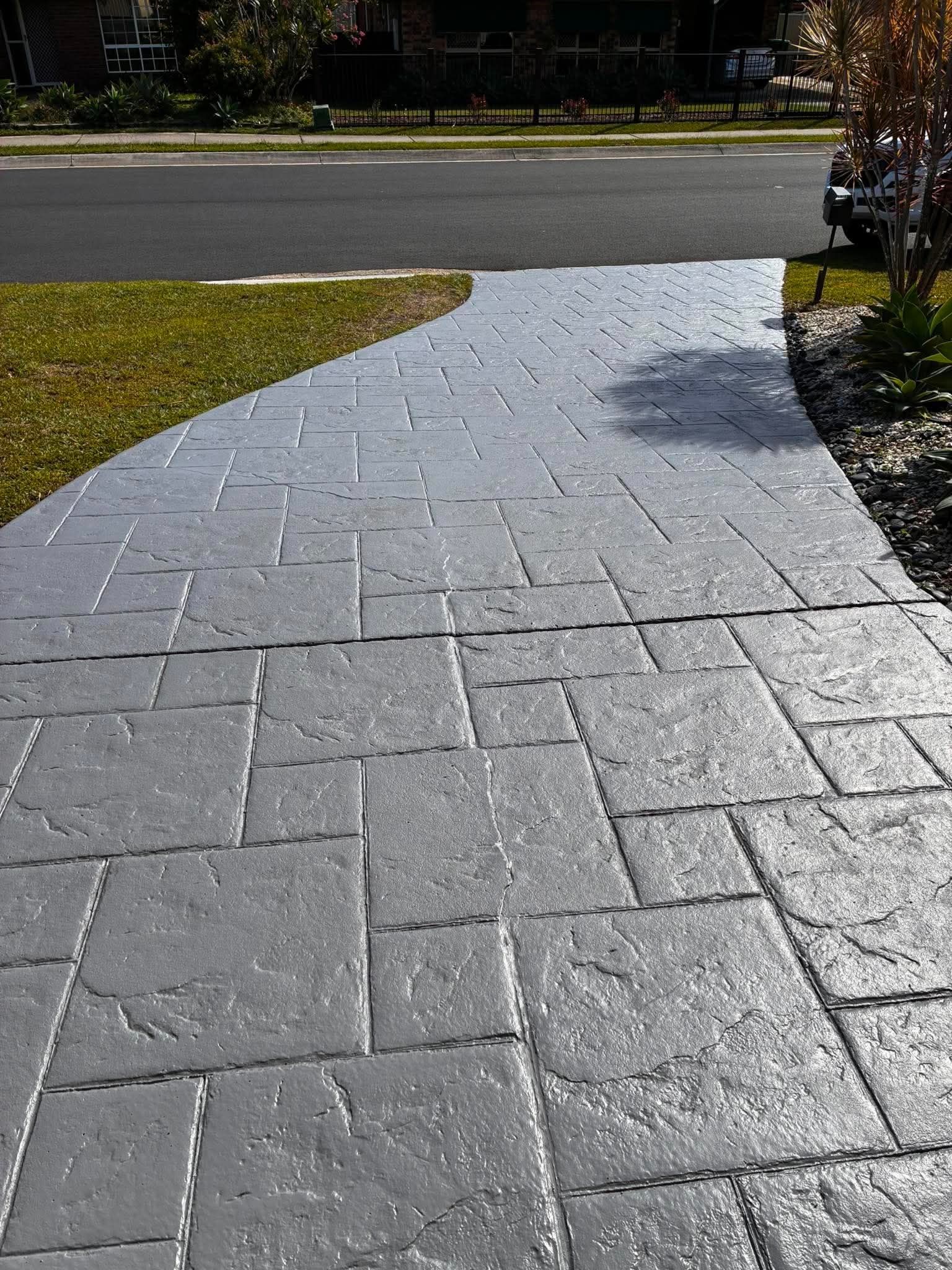 Brick walkway leading to a road, with grass along the left edge and a tree on the right.