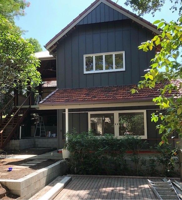 Two-story dark gray house with red roof, front porch, and steps leading to a garden courtyard.