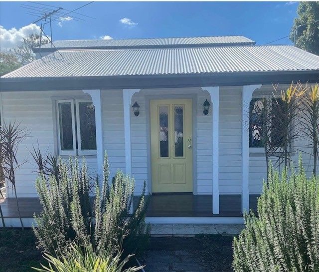Small white house with a yellow front door, porch columns, and tall plants in front