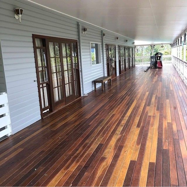 Covered porch with polished hardwood floor, white siding, and French doors along the side of a house.