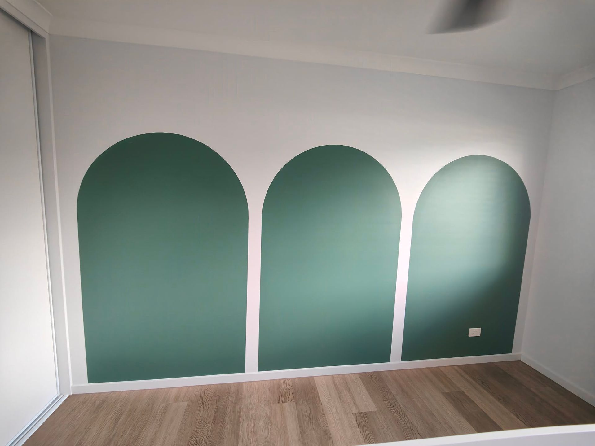 Empty room with three dark green arched wall panels and wood flooring