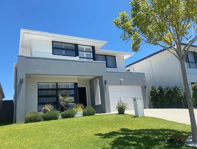 Modern two-story white house with a green lawn, large windows, and a tree in front under a clear blue sky