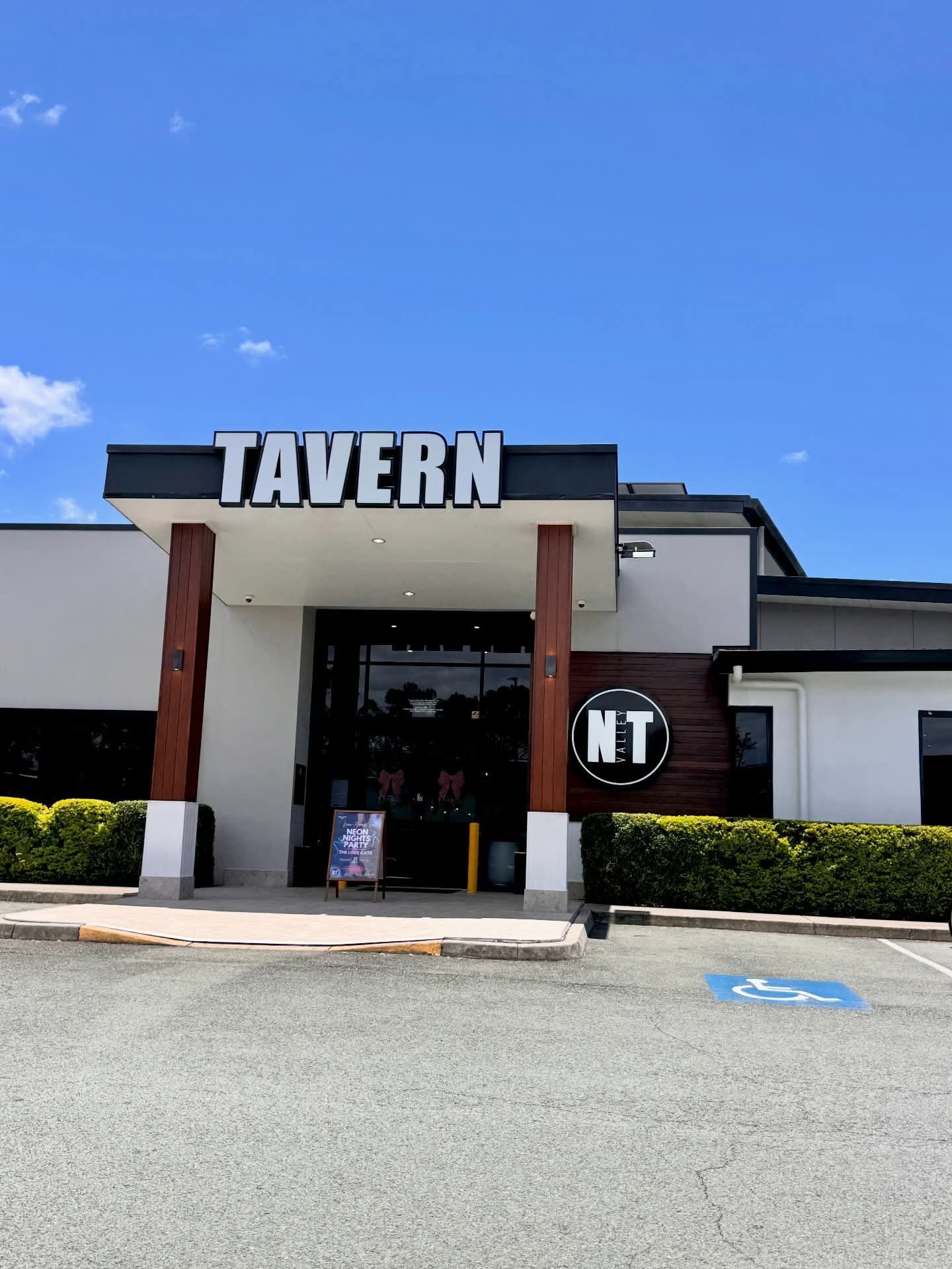 Front entrance of a tavern with bold TAVERN sign, white facade, and blue sky overhead.