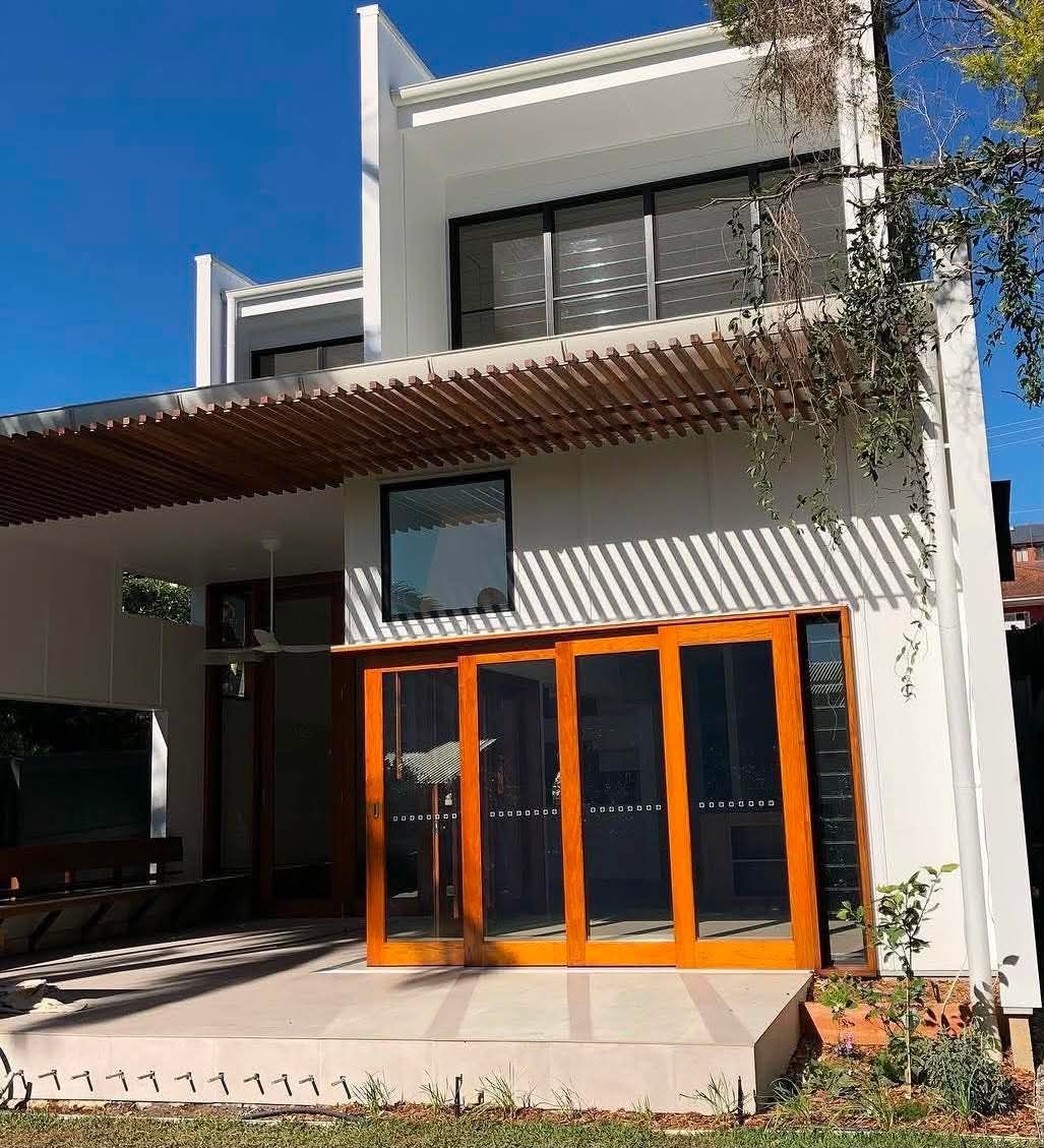 Modern two-story white house with orange-framed glass doors and a shaded front porch