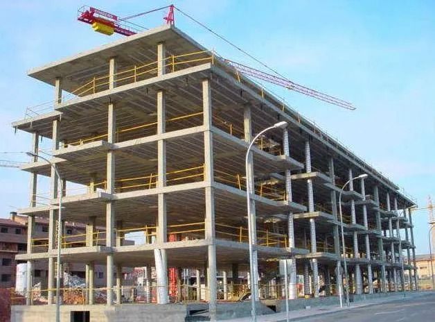 Estructura de hormigón parcialmente construida con andamios y una grúa roja en el tejado.