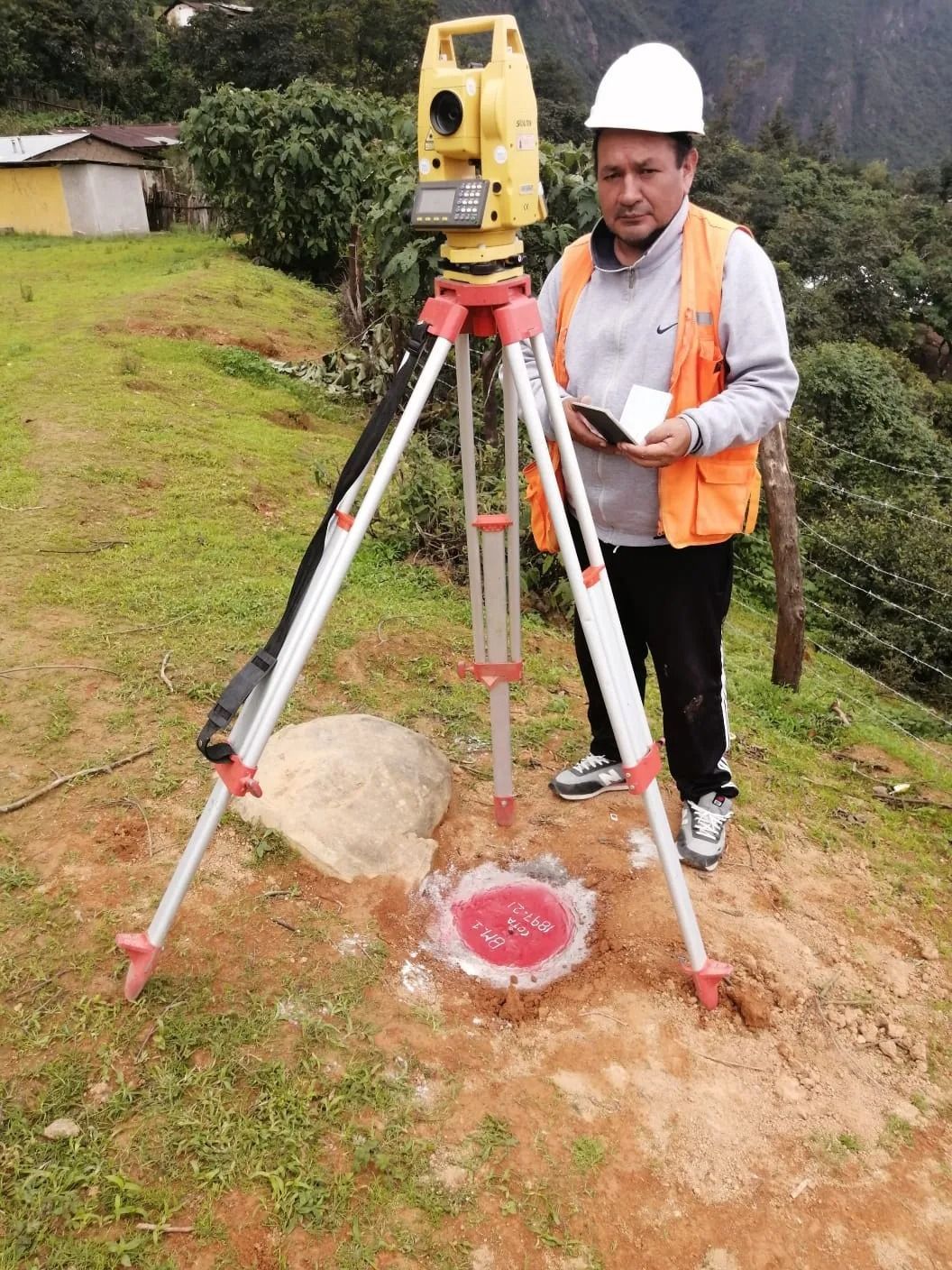 Topógrafo con casco y chaleco naranja utilizando un instrumento montado sobre trípode al aire libre 