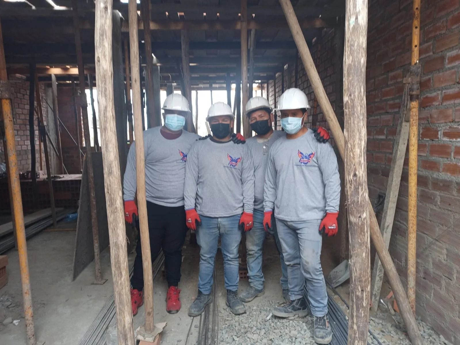 Cuatro trabajadores con cascos y mascarillas permanecen de pie en el interior de un edificio de ladrillo sin terminar.